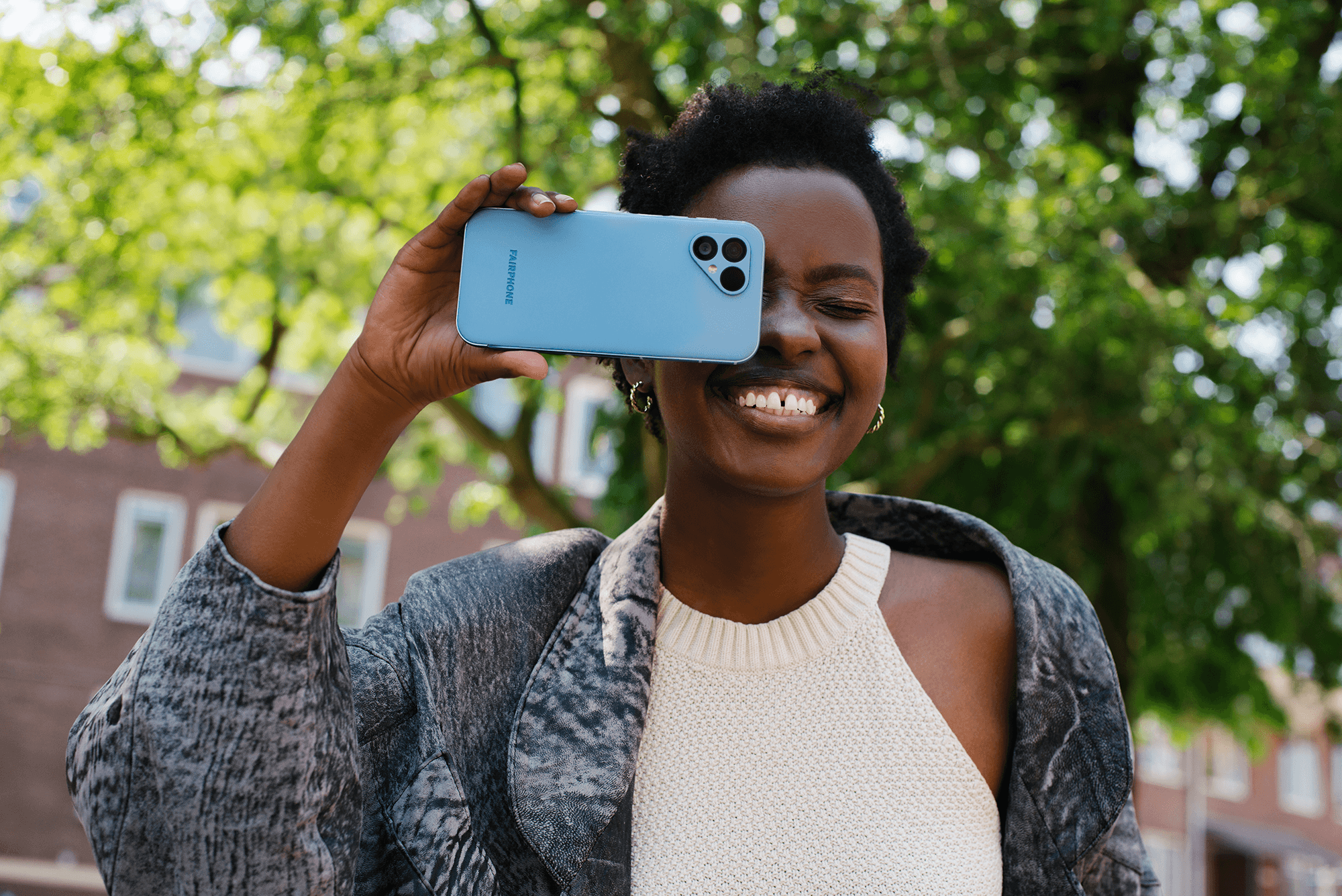 Lachende vrouw houdt Fairphone voor haar rechteroog
