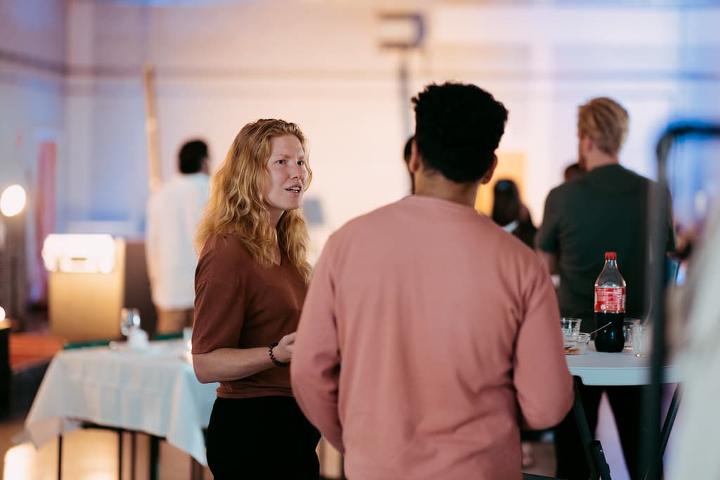 en foto van een bijeenkomst bij Waag Futurelab. Een vrouw met lang rood haar is in gesprek met een man met kort zwart haar en een roze trui, die met de rug naar de camera gekeerd staat.